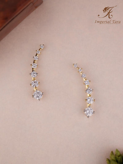 Pair of gold and diamond earrings on a beige background with 'Imperial Tara' branding.